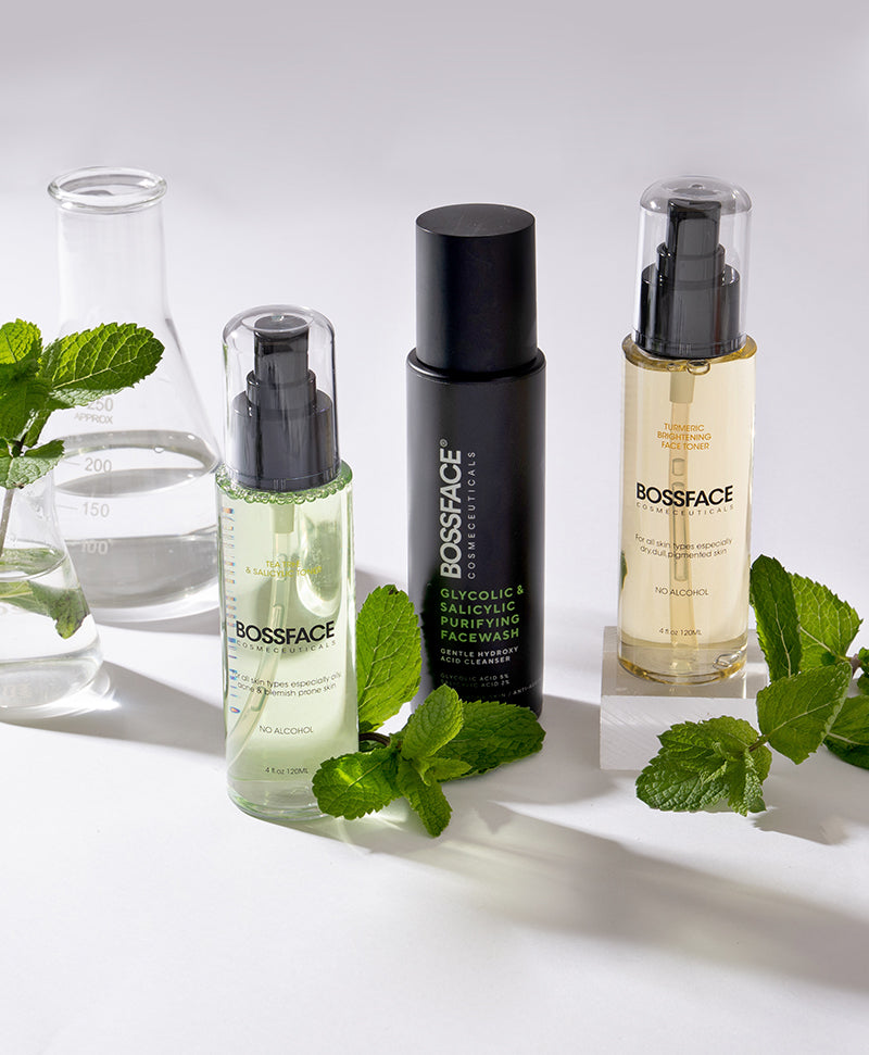 two clear bossface toner bottles filled with a green liquid and one with green liquid, lying along side a black bossface bottle of facewash