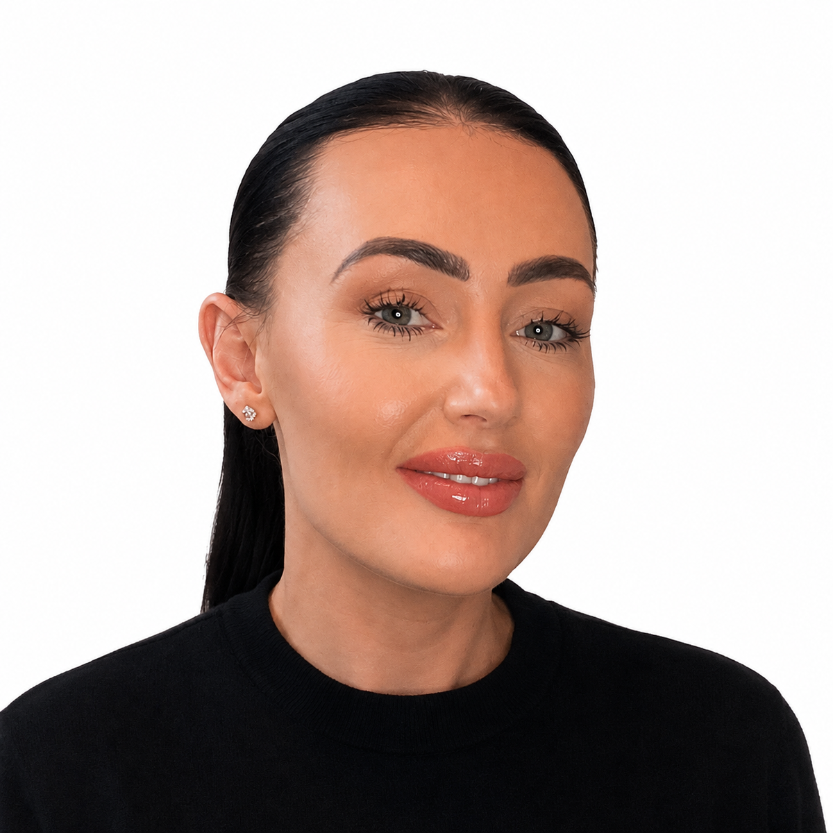 A close-up portrait of a woman with dark hair pulled back, wearing a black top and a small silver stud earring, set against a plain white background.