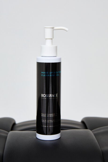 a black bottle with Make up melting cleansing oil written in blue on the label. Bottle is on a black stool